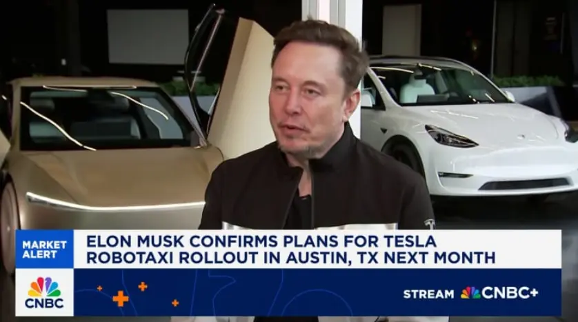 A screenshot from a CNBC segment featuring Elon Musk being interviewed in front of two Tesla vehicles (one with its gull-wing door open).