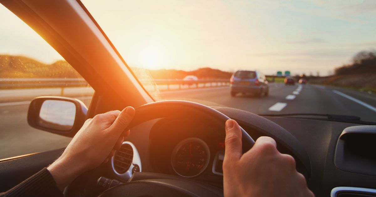 Driver's hands on the steering wheel on a highway at sunset, illustrating self-driving vehicle accidents