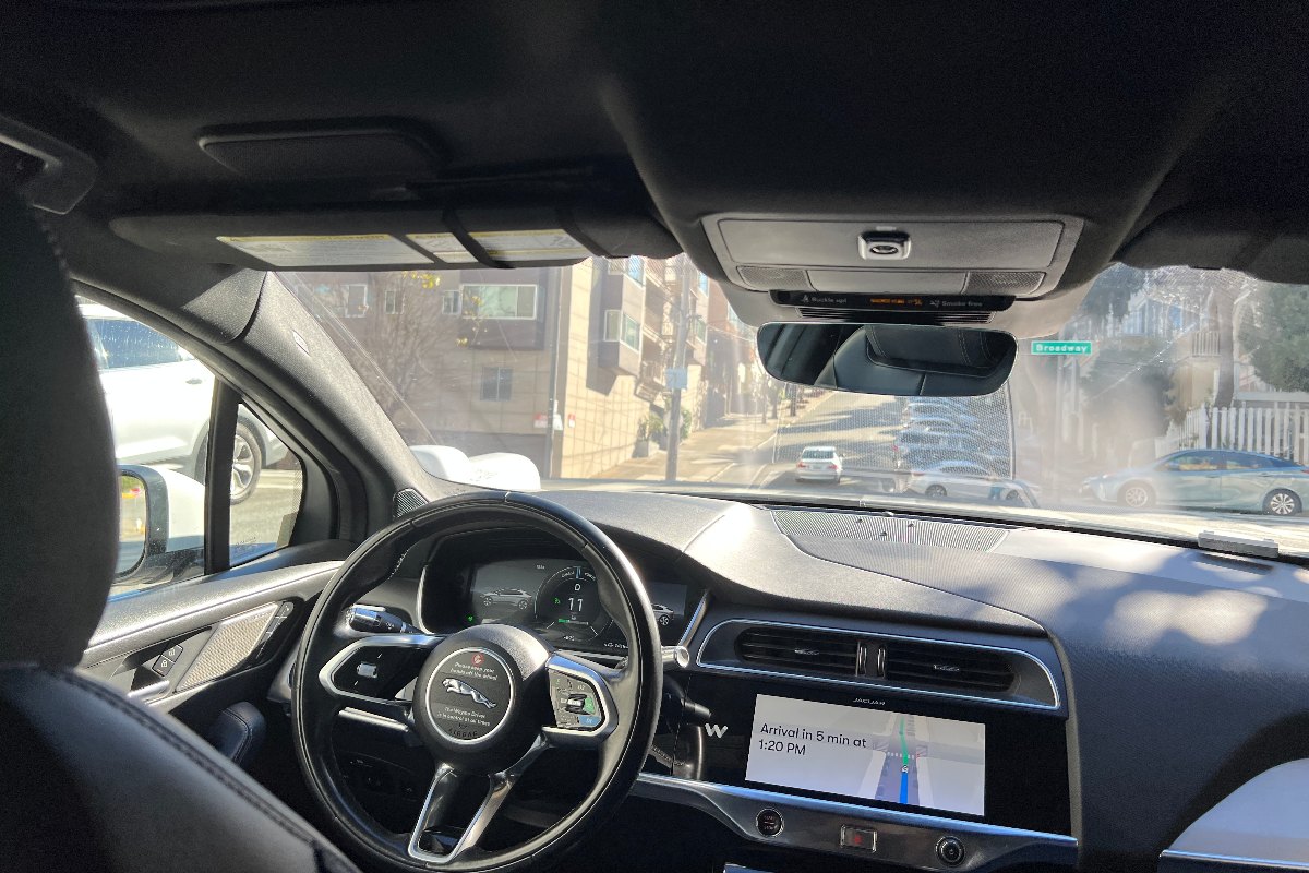 Interior of a self-driving rideshare vehicle showing the empty driver's seat and dashboard screen