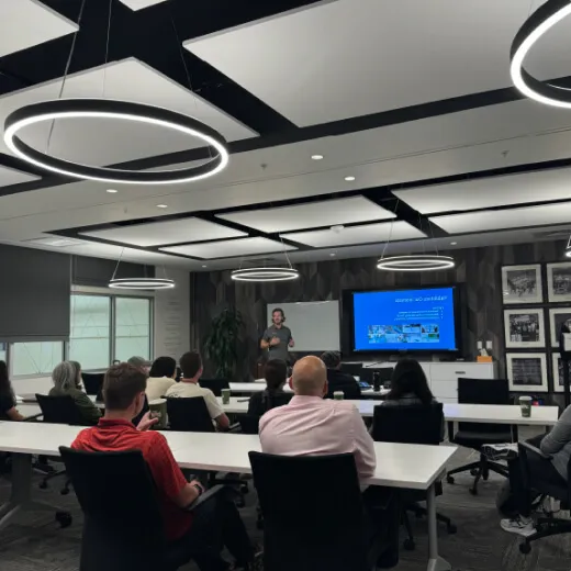 A professional setting with a speaker presenting to an audience. Modern conference room with circular lights and a screen display.