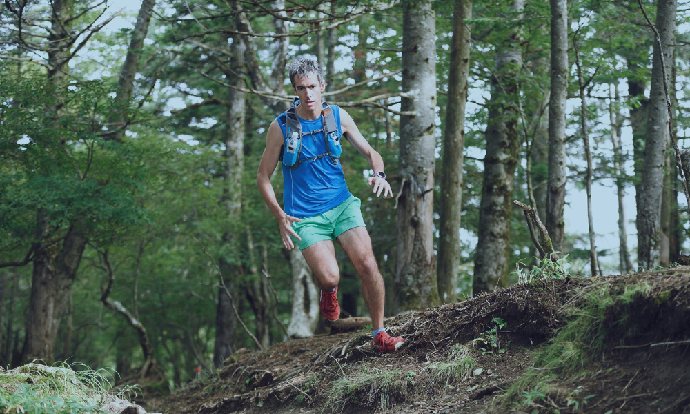 Male trail runner descending a forested slope