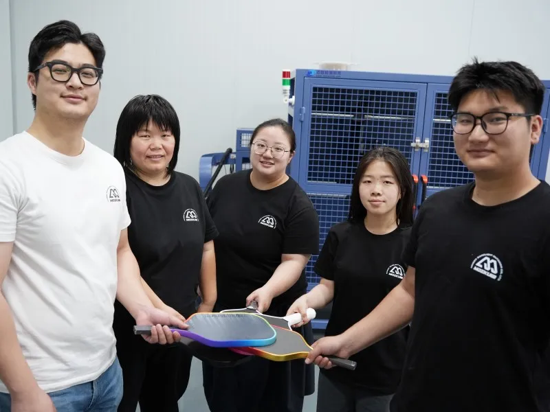 Mozkuib team holding pickleball paddles inside the factory