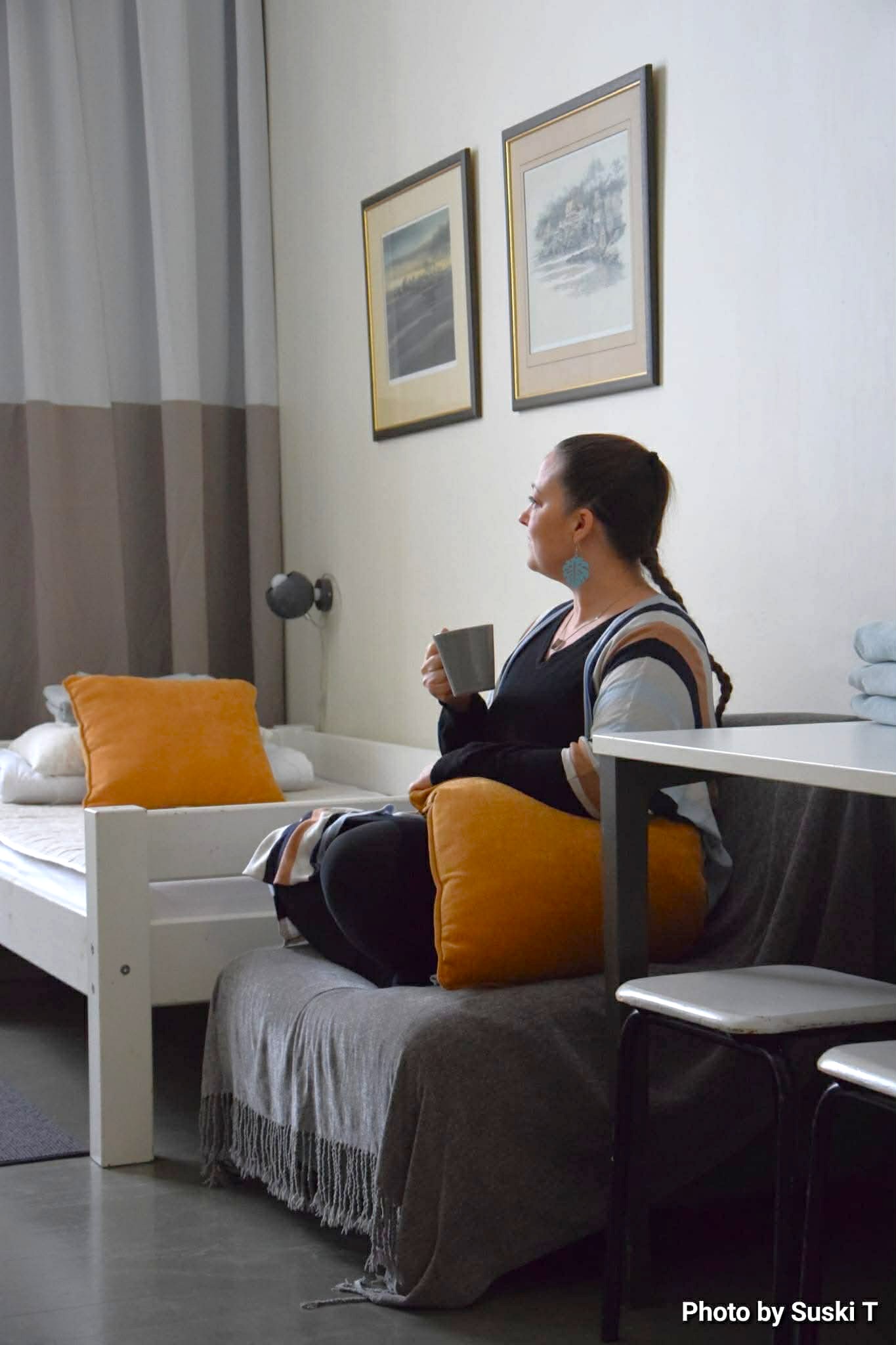 A guest sitting on the bed with a mug in the room