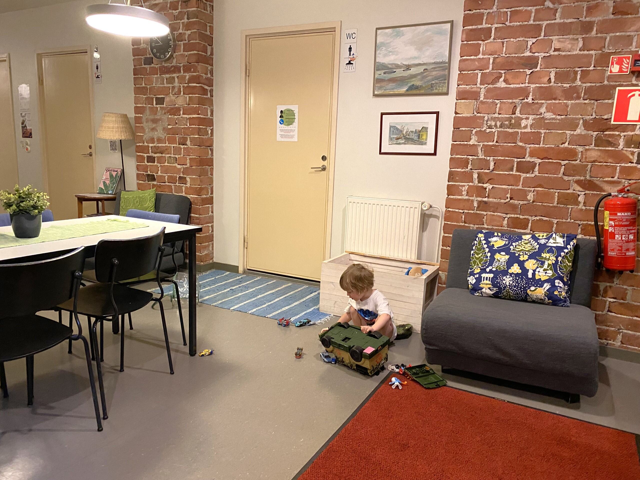 A child playing with toys on the lobby floor, brick wall in the background