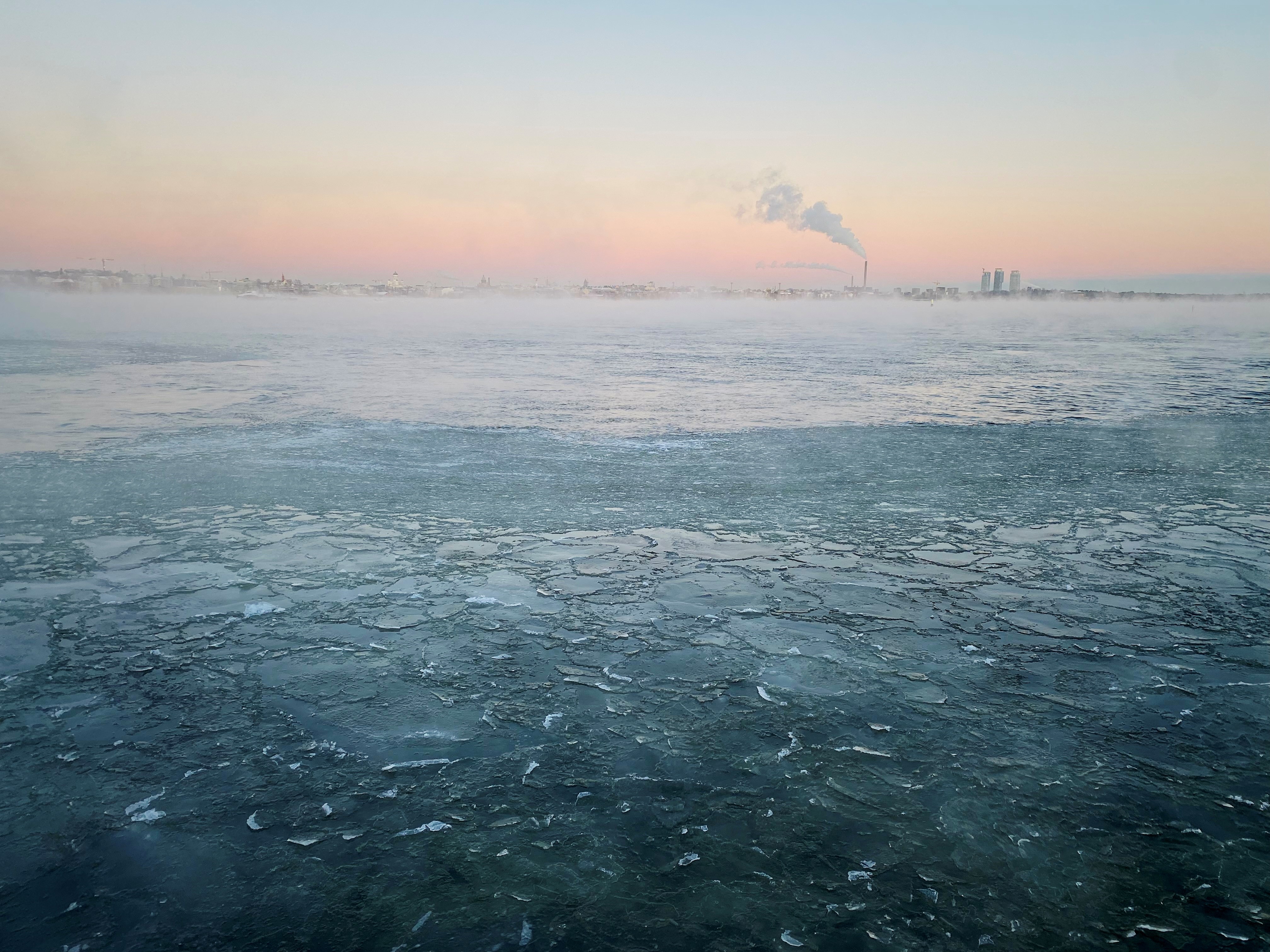 Steaming winter sea with ice floes, city skyline in the background