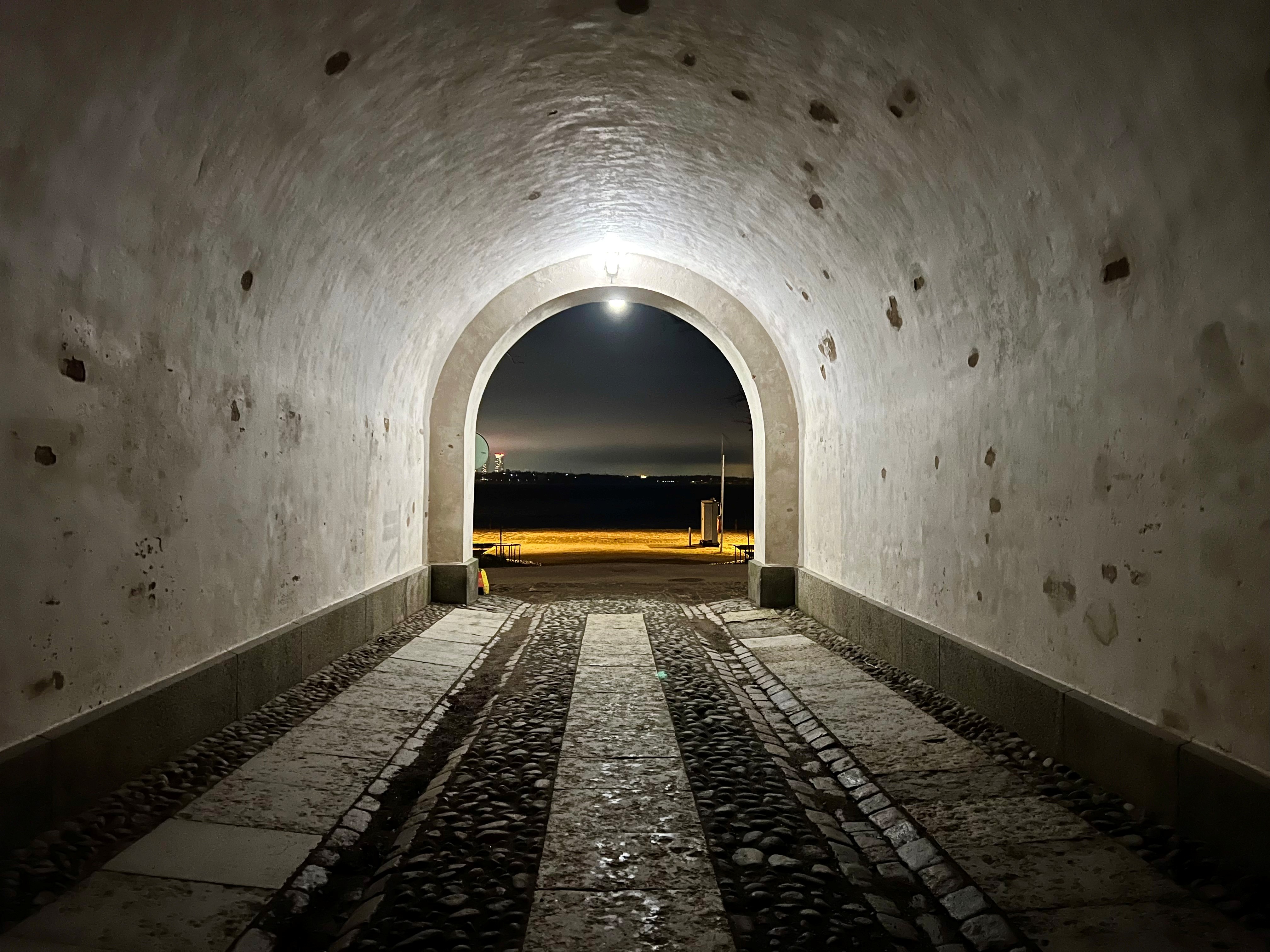 Lit vaulted tunnel and cobblestone passage in the evening