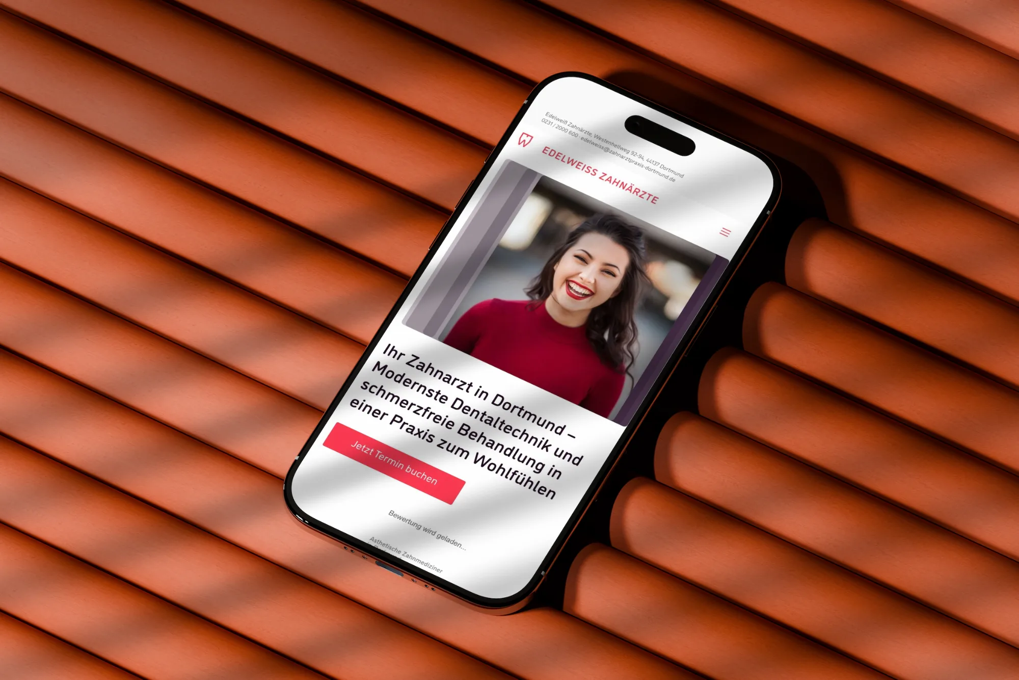 Smartphone mit der Website der Edelweiß Zahnärzte auf Dachziegeln