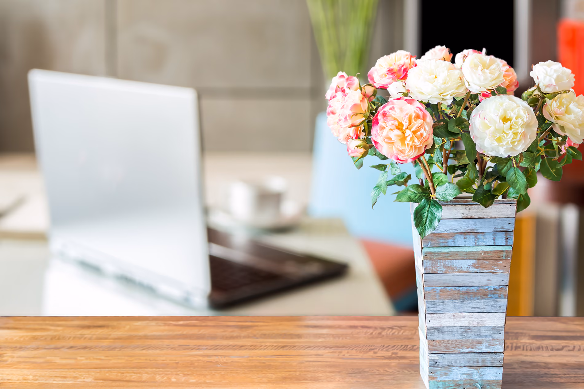 A vase of colorful flowers sits on a table in front of an open laptop, creating a vibrant workspace atmosphere.