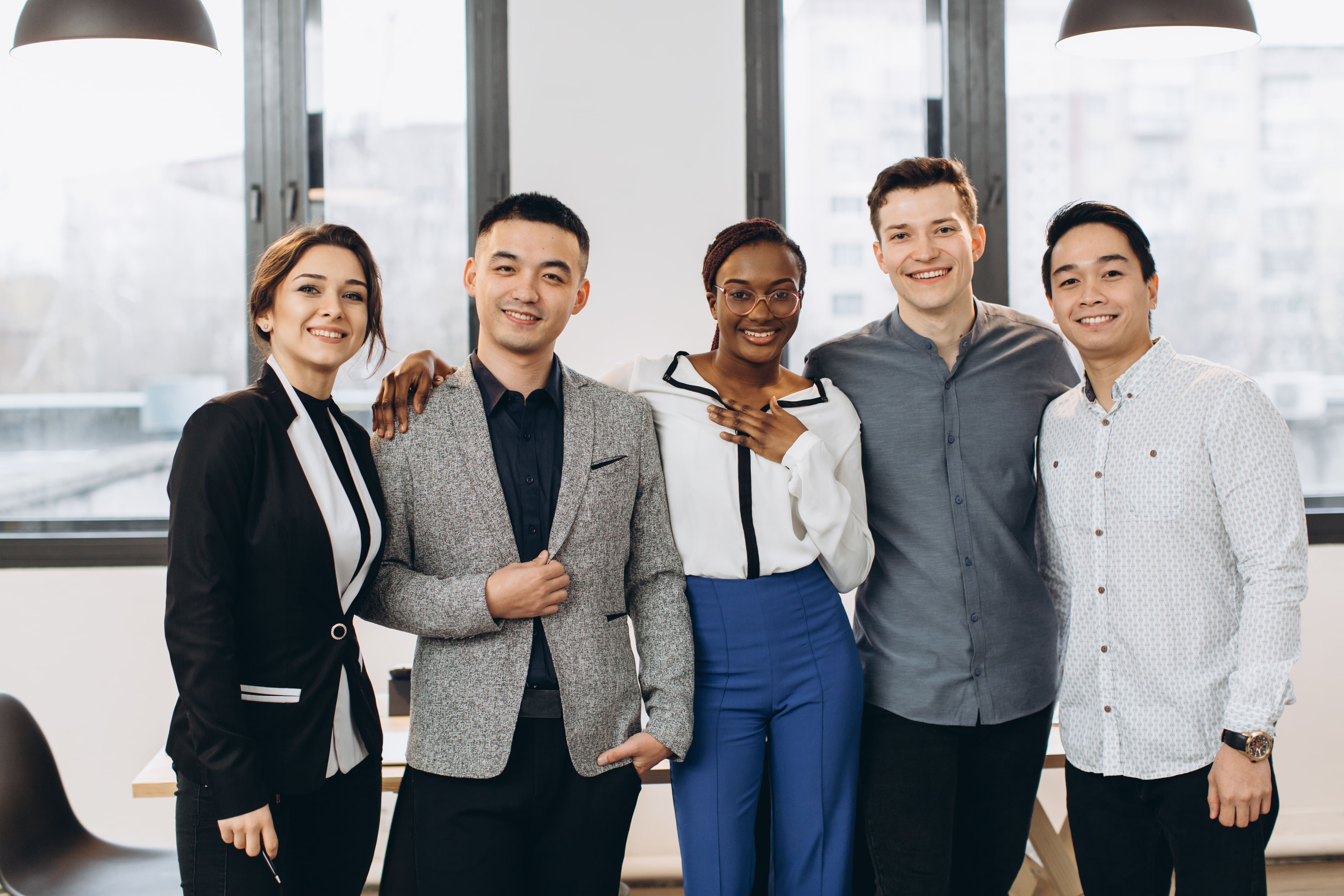 A diverse group of five smiling professionals standing in a modern office, symbolizing a dynamic recruitment agency team.