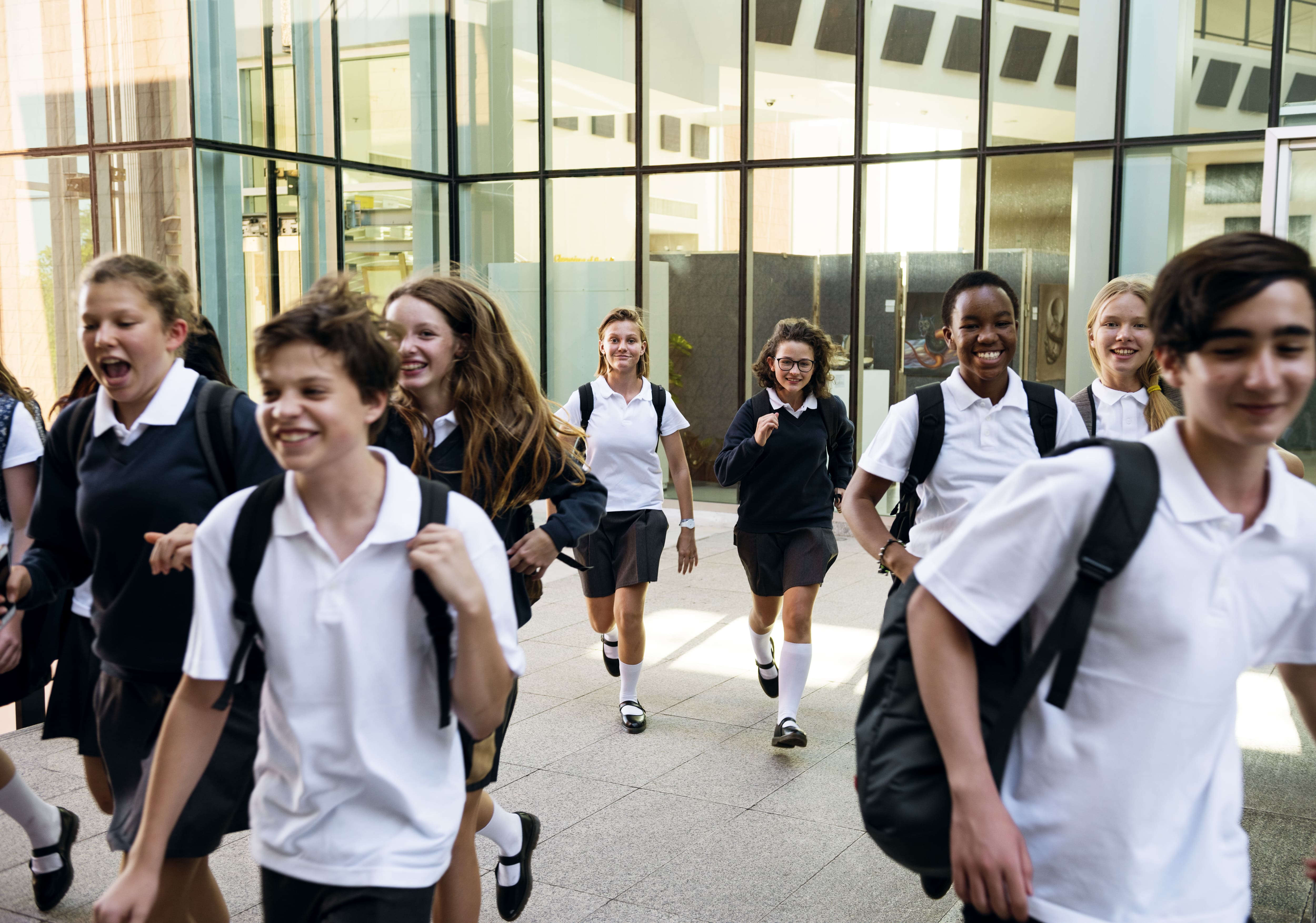 A diverse group of cheerful private school students in uniform walking together outside a modern school building, conveying an energetic academic environment.