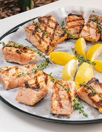Grilled salmon fillets garnished with fresh thyme and lemon wedges on a round platter.