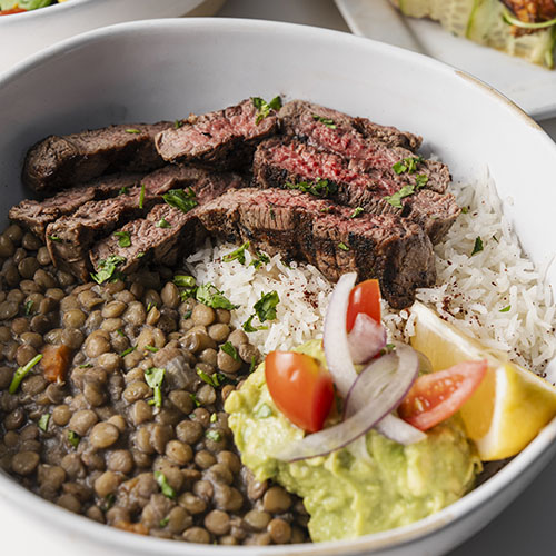 Grilled salmon fillet served with white rice, lentils, a dollop of avocado salsa, and a lemon wedge in a bowl.