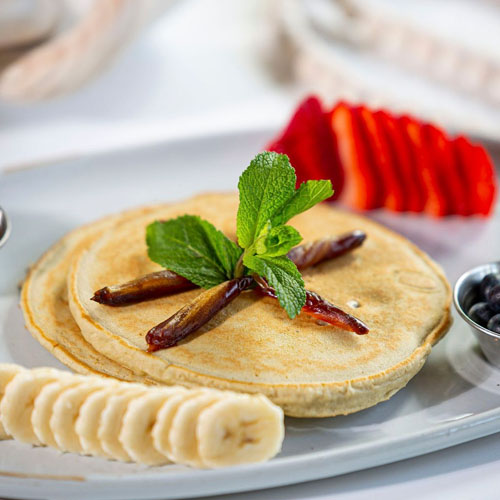 Bowl with four falafel balls, white rice, guacamole, lentils, chopped herbs, and a lemon wedge.