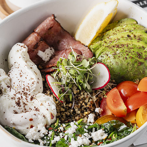 Bowl with sliced grilled steak, white rice, lentils, guacamole, and a lemon wedge garnished with herbs.