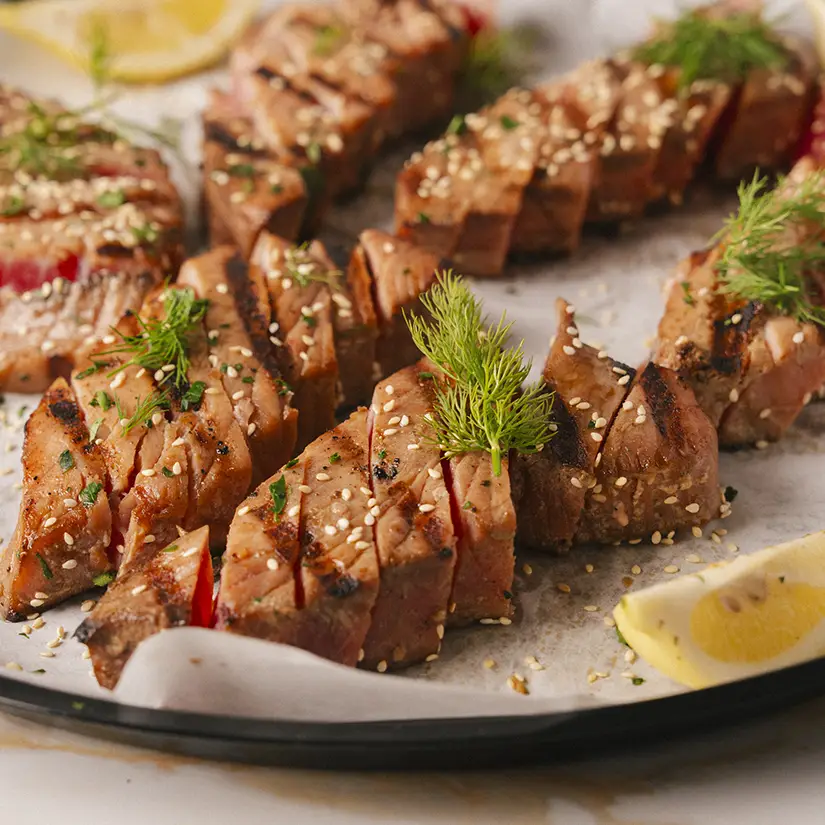 Interior of a modern café with white tables, wooden chairs, hanging plants, and a counter where customers are ordering.
