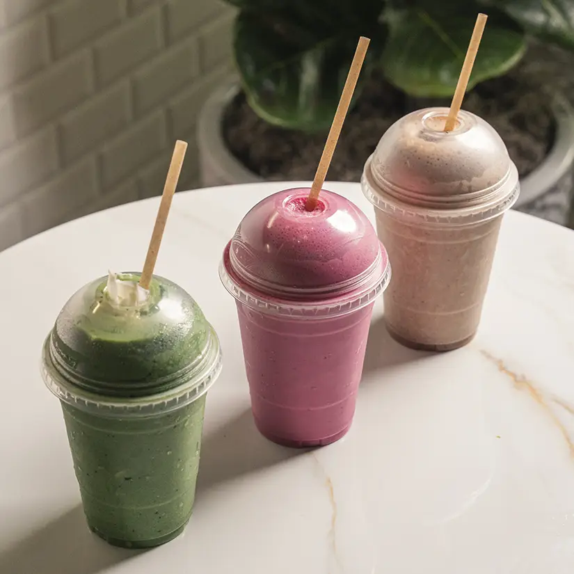 Modern cafe counter with breads and pastries behind glass, two water dispensers on countertop, wooden stools, and staff preparing orders.