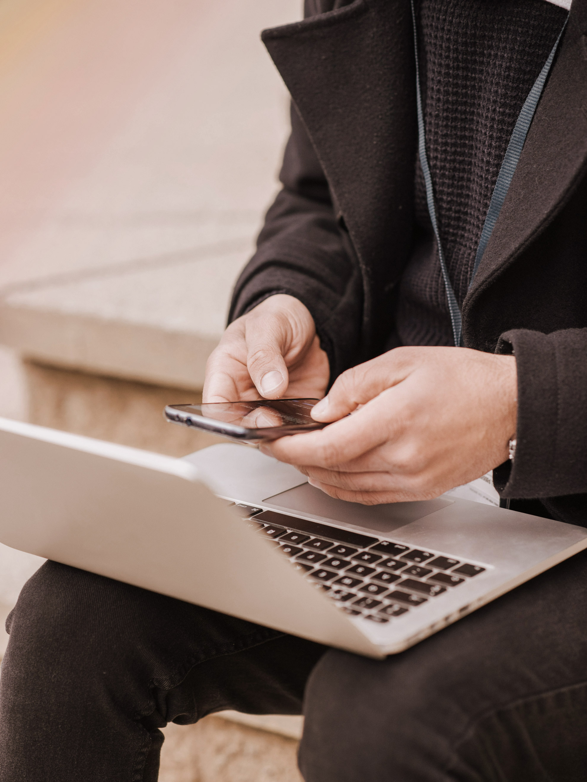Person sitzt draußen und nutzt simultan Smartphone und Laptop auf dem Schoß.