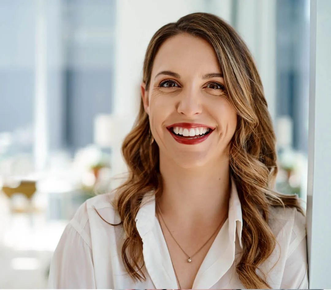 Smiling woman with long wavy hair looking at the camera in a bright office environment.