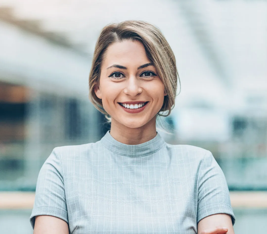 Smiling professional woman with short hair, standing with arms crossed in a bright office setting.