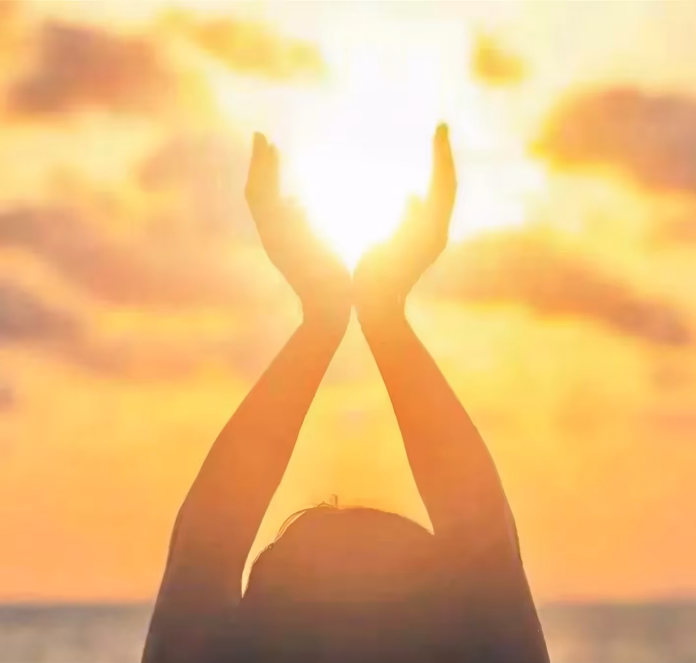 Person holding hands up as if cupping bright sunlight during a golden sunset.