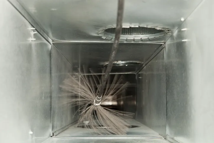 This image provides a close-up, internal view of a metal air duct during a cleaning process.