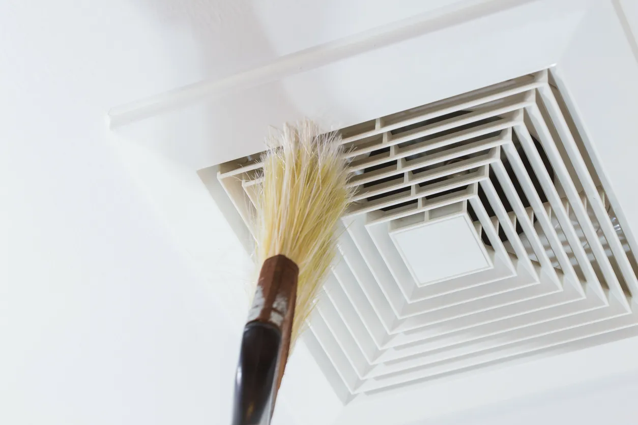 Technician inserting red hose into ceiling vent, cleaning air duct.