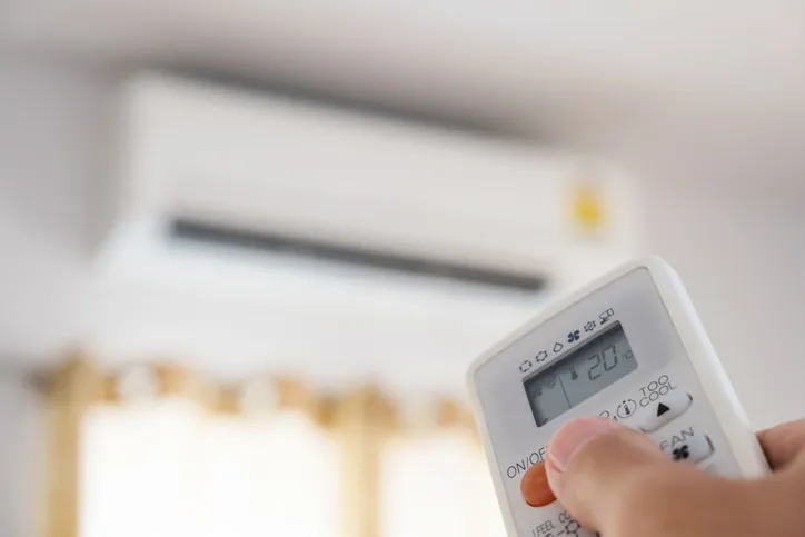 Person aiming remote control at wall-mounted air conditioner, display partially visible