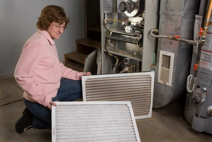 Woman holding a dirty and clean furnace filter next to an open furnace.