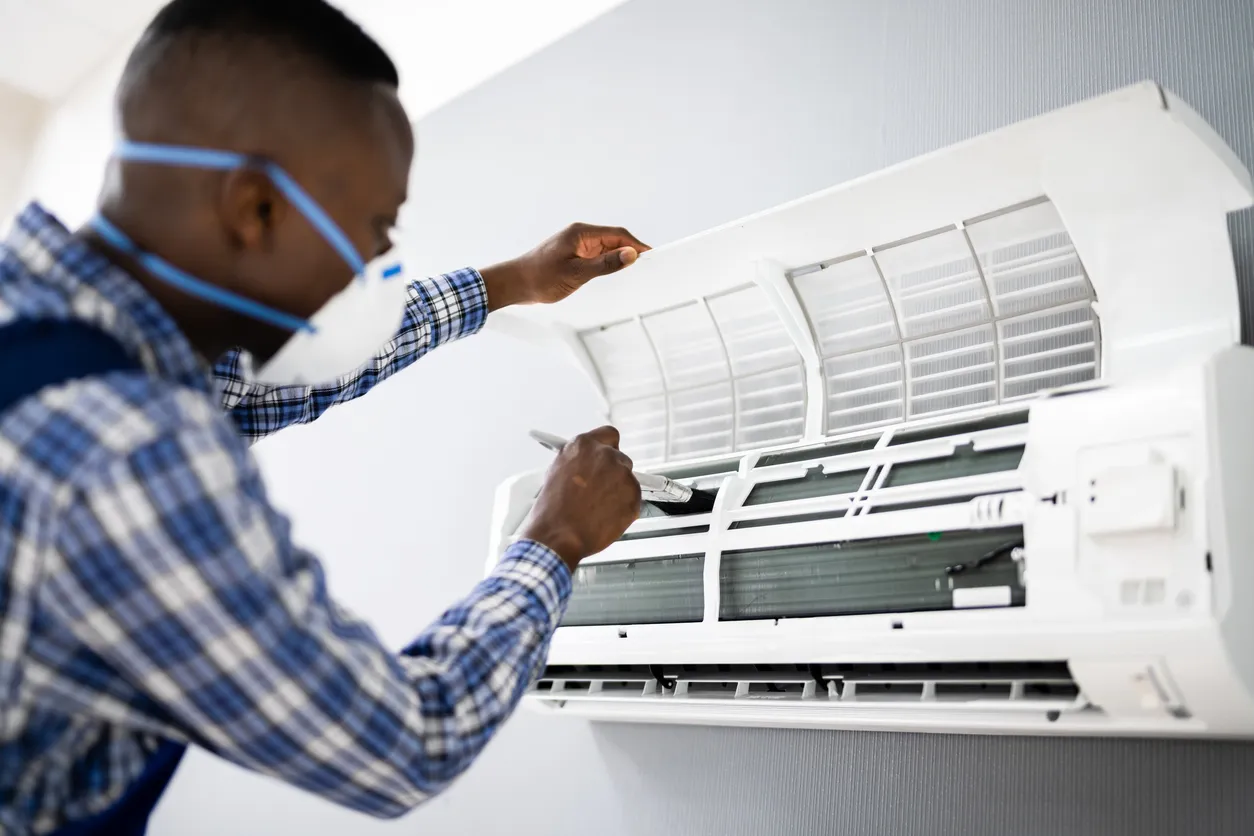 Technician in checkered shirt servicing wall-mounted air conditioner, lifting front panel for maintenance