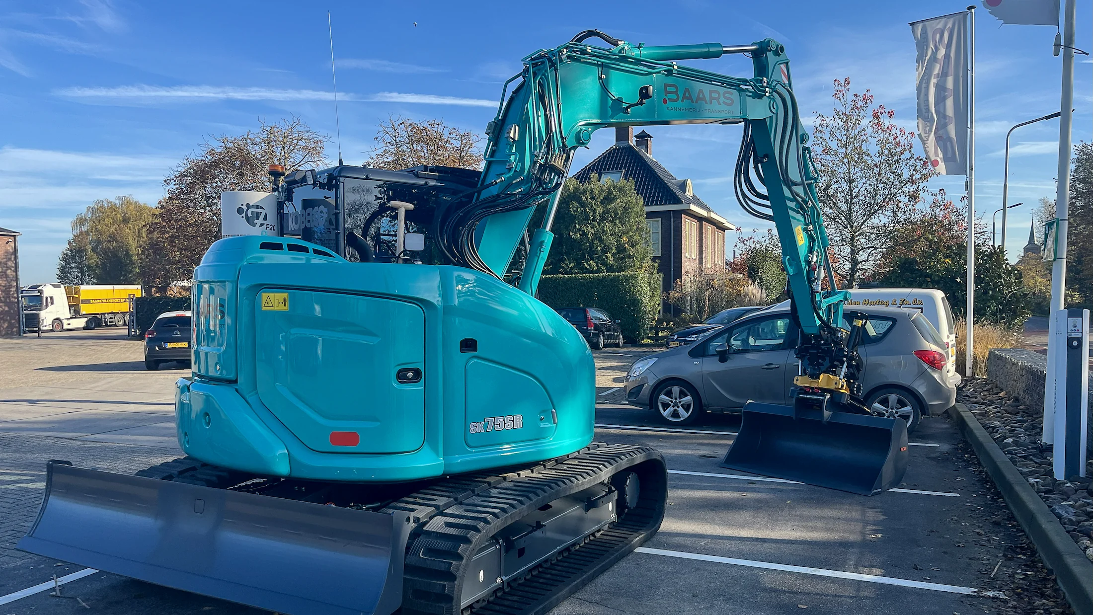 Zijaanzicht van de nieuwe Kobelco SK75SR midigraver van Baars met Engcon draaikantelstuk, geparkeerd op het terrein bij aflevering.