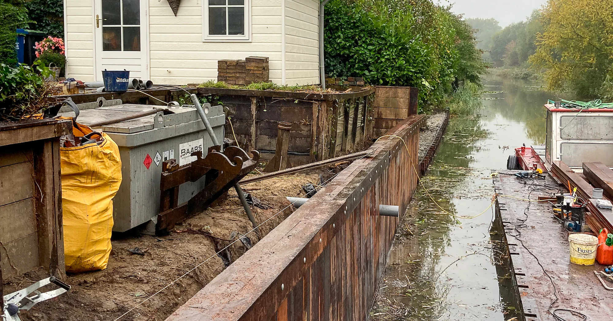 Afgewerkte houten damwandconstructie naast woonhuis aan het water