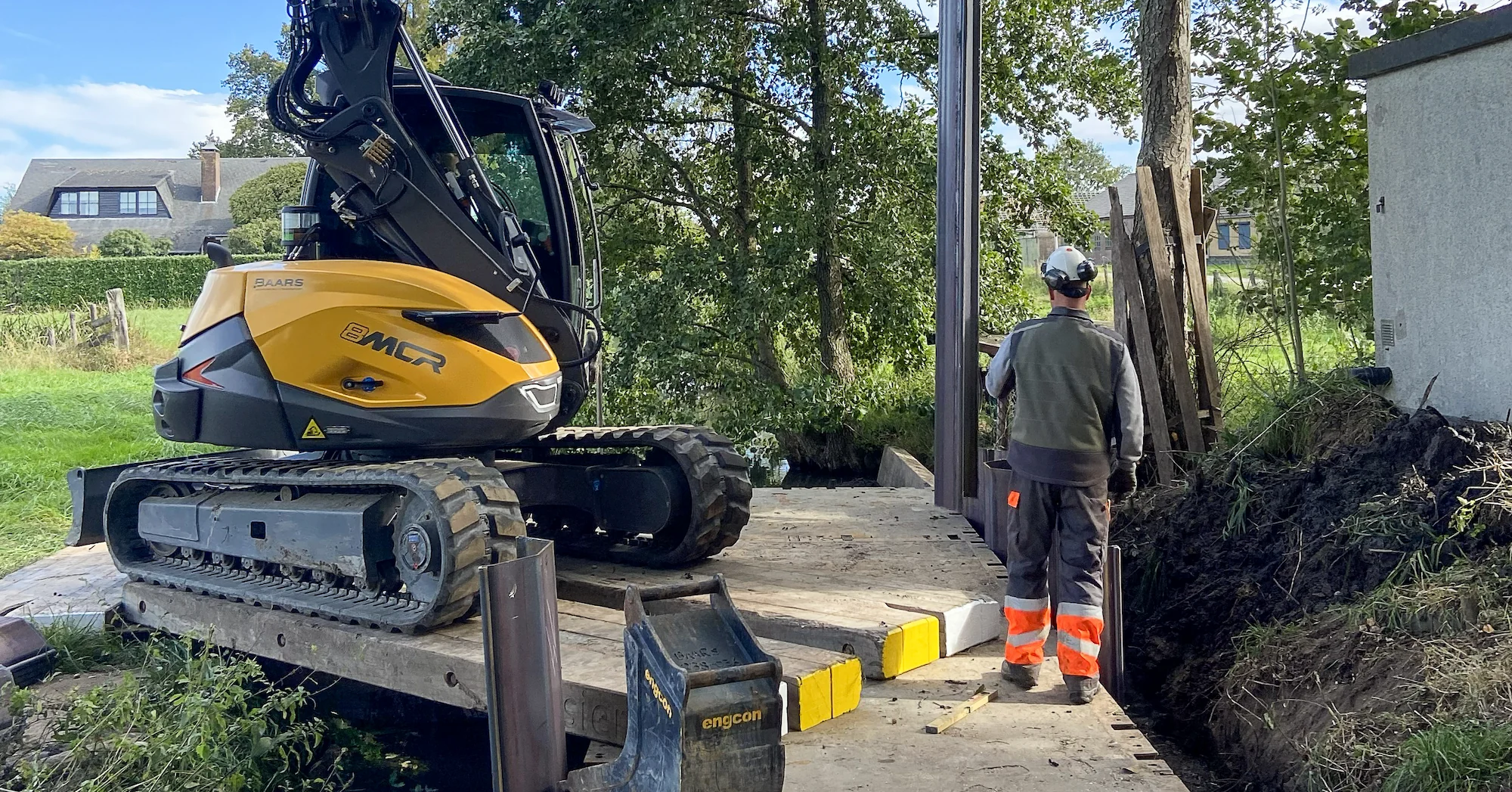 Medewerker brengt stalen damwand aan vanaf ponton met Mecalac midigraver