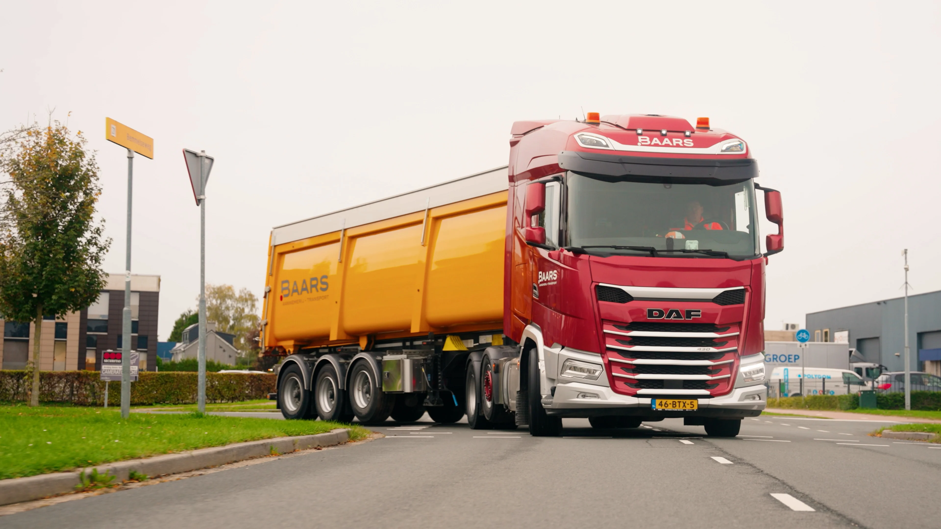 Rode Baars vrachtwagen met gele kipper rijdt door een bocht op een industrieterrein tijdens transportwerkzaamheden