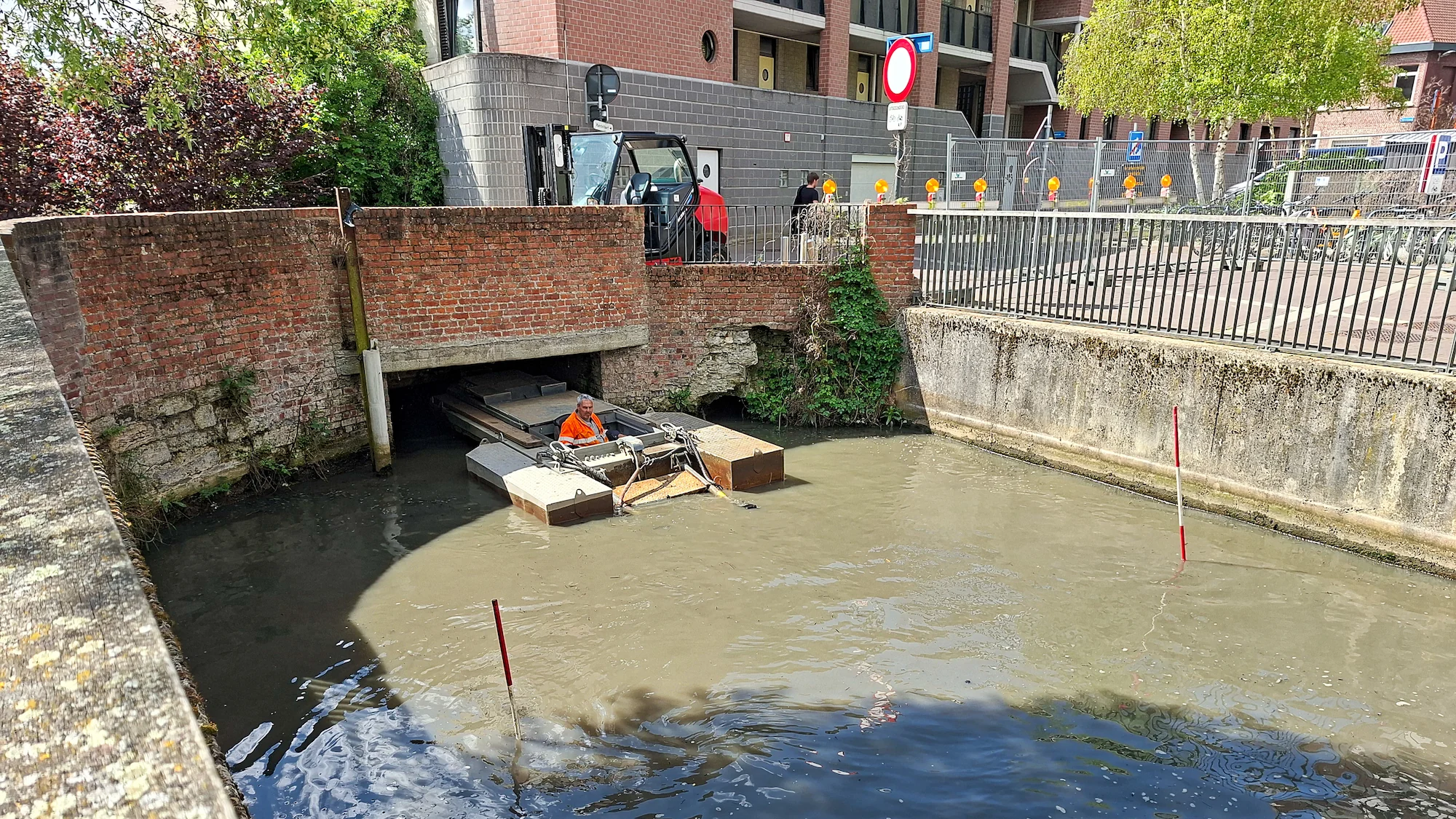 Baggerwerkzaamheden met kleine baggerboot onder brug in stedelijke watergang in België