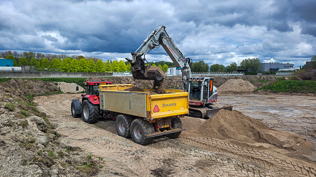 Grondtransport binnen het baggerdepot. Een rupskraan laadt een dumper met grond die wordt gebruikt voor het opzetten van de depotkade en het modelleren van het terrein.