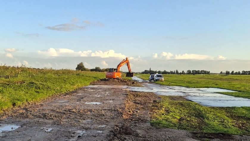 Graafmachine aan het werk op een rijplatenpad langs de kade bij de kadeversterking Smoutjesvliet in Goudriaan.