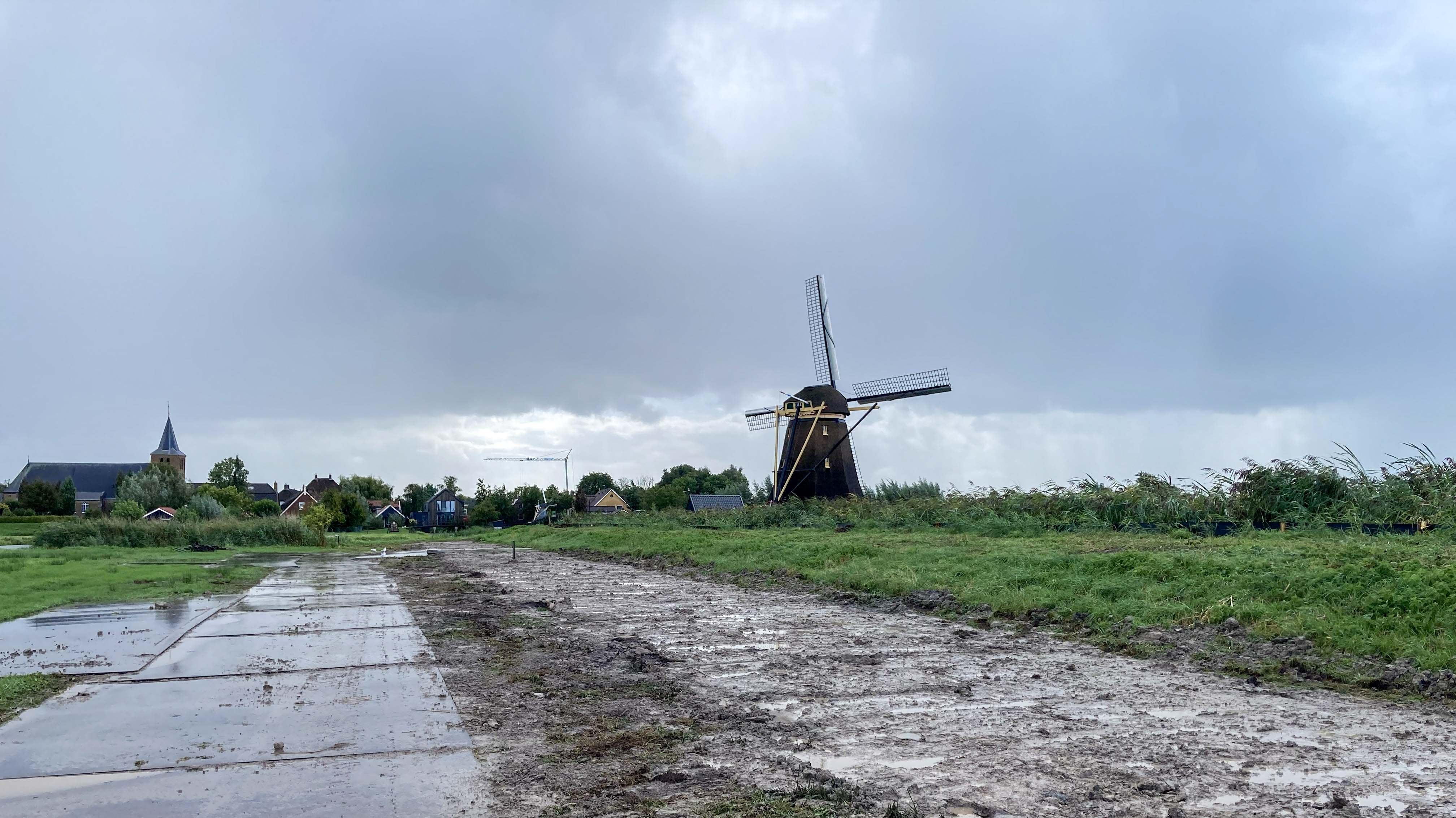 Bewerkt terrein met rijplaten langs de kade bij Goudriaan, met een molen en dorpsbebouwing op de achtergrond.