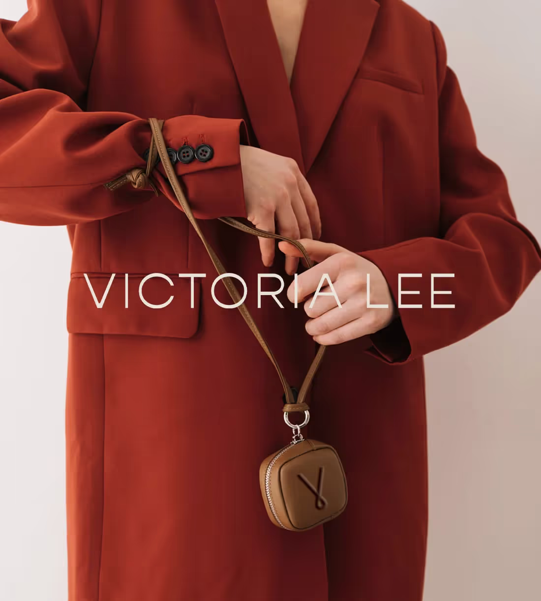 Image of a woman in a red coat holding onto a leather clutch with the brand Victoria Lee designed by Saevil Row