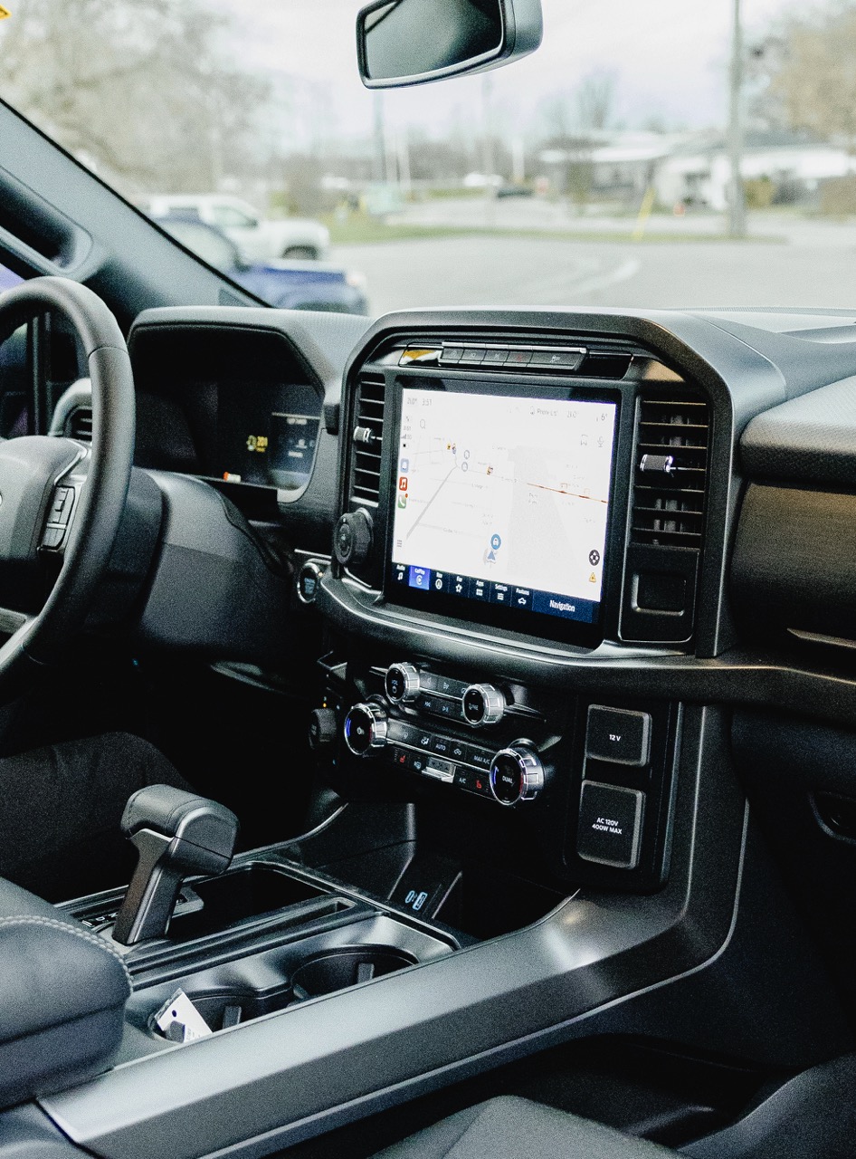 Interior of a modern vehicle showing the steering wheel, gear shift, and a central touchscreen displaying a navigation map.