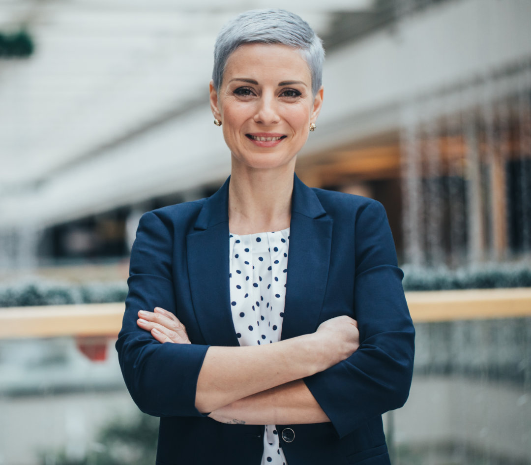Confident woman with blonde hair, folded arms, and smiling.