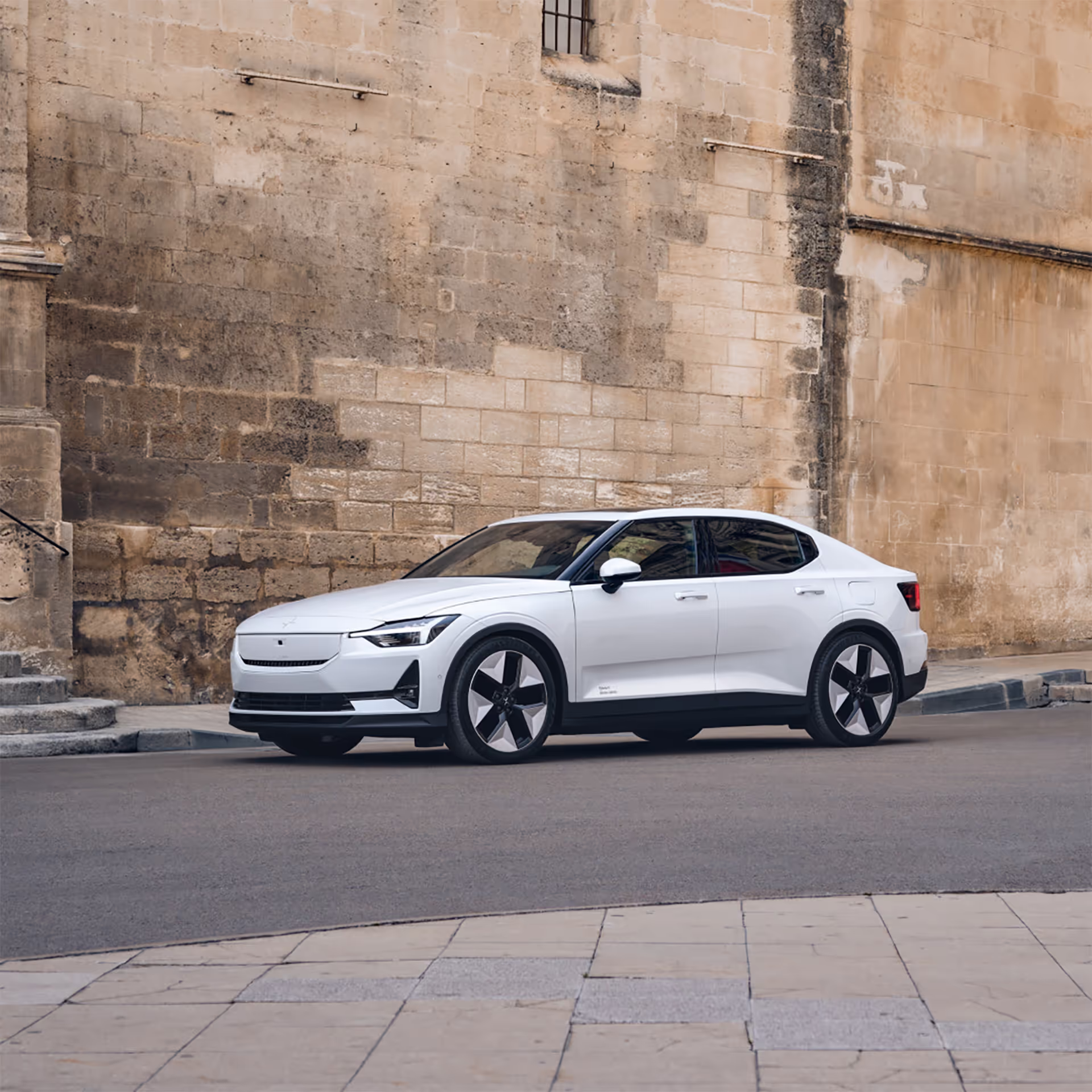 A sleek white sedan parked on a quiet urban street, set against a backdrop of a weathered stone wall with subtle architectural details.