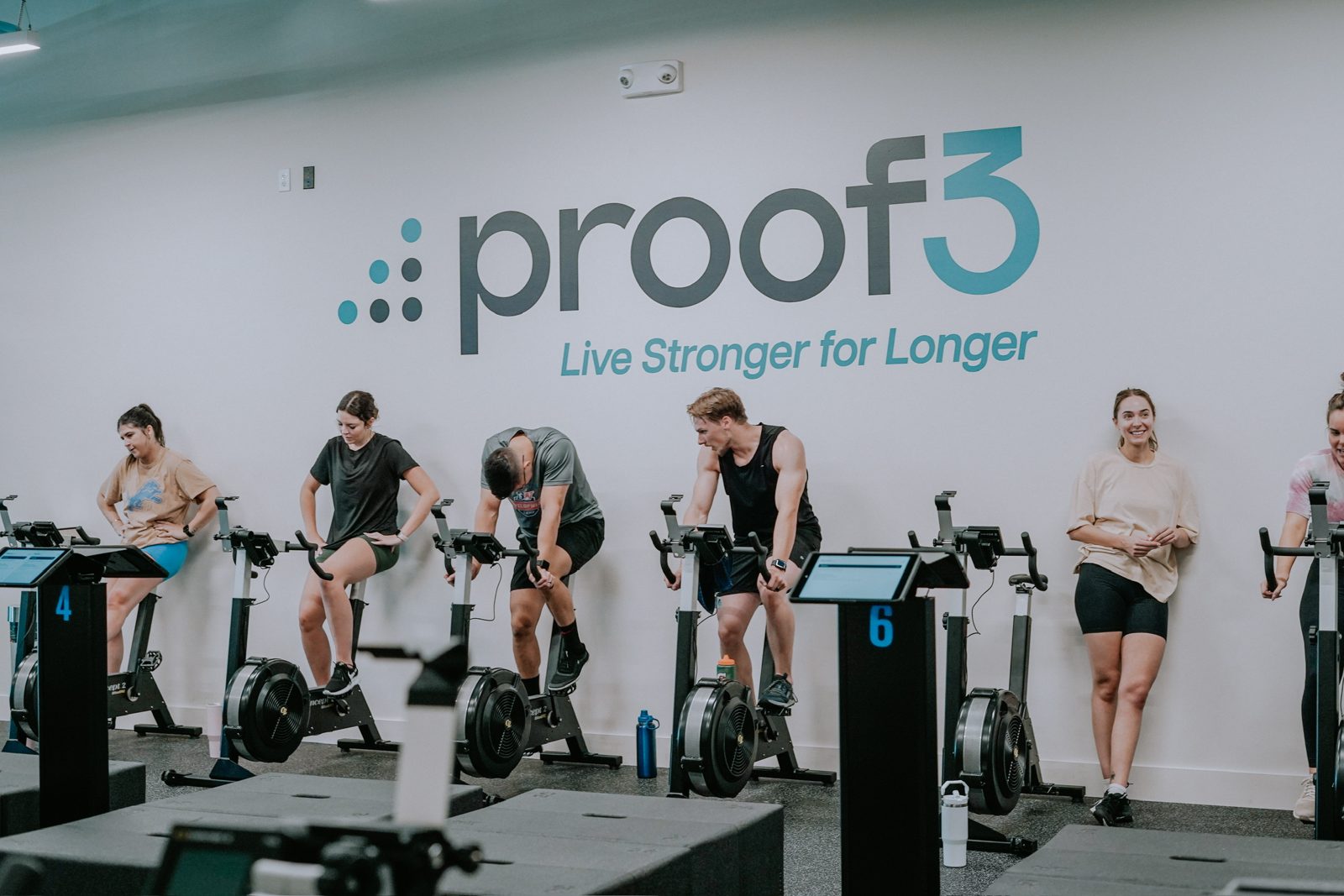 Members train on exercise bikes in front of the proof3 wall during a group session.