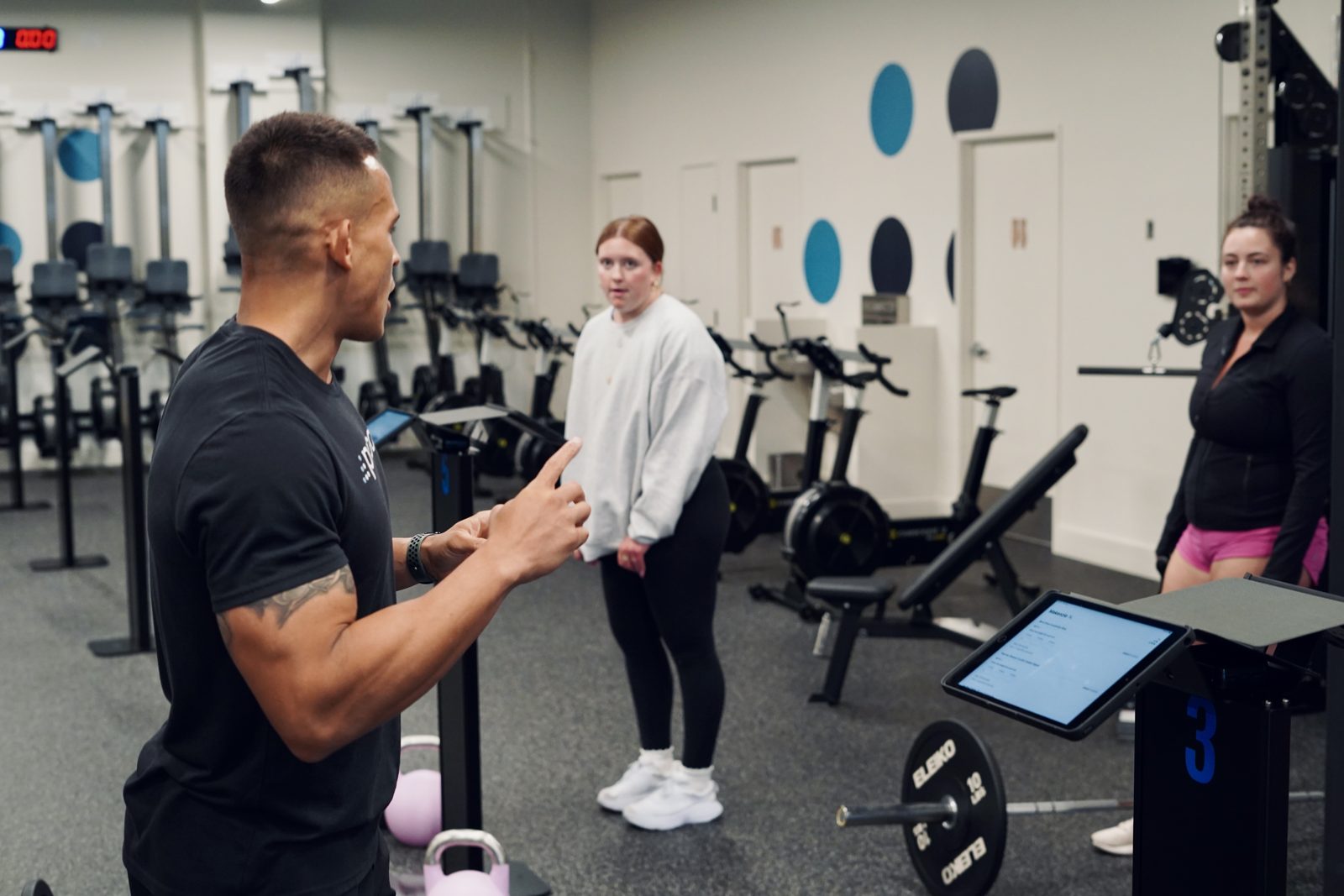 A proof3 coach explains an exercise to two members on the gym floor.