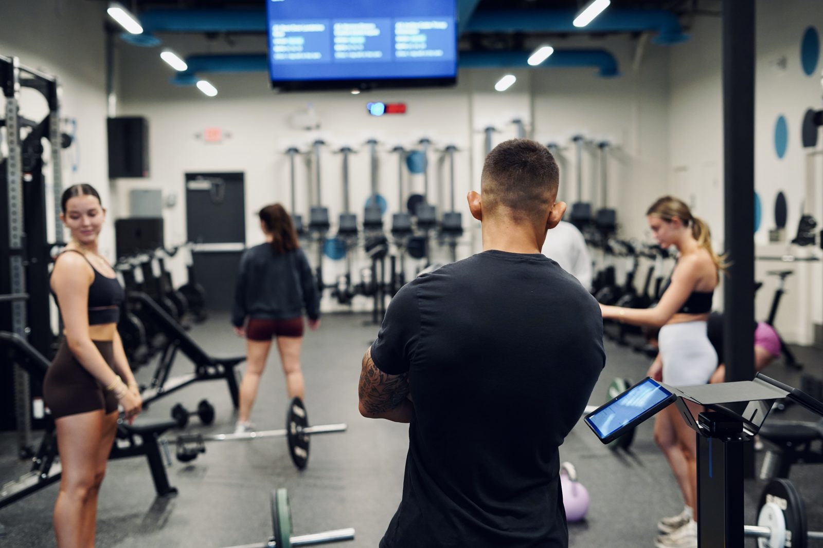 A proof3 coach checks in with members as they train across the gym floor.