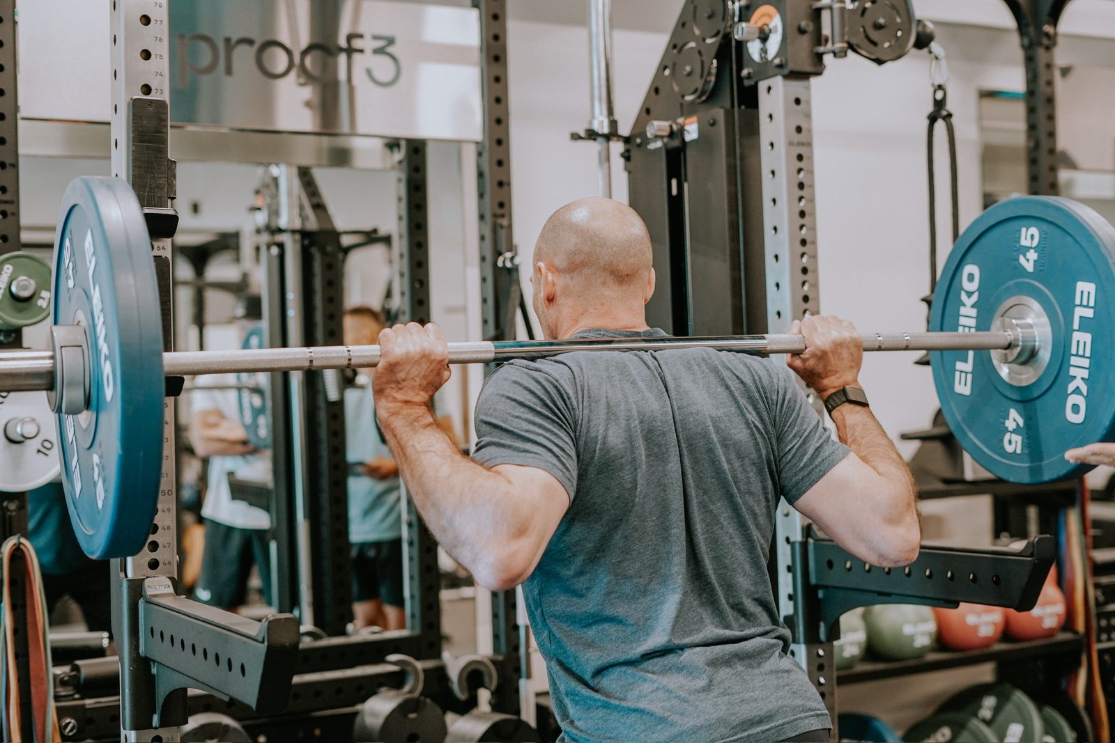 A member lifts a barbell in a squat rack at proof3.