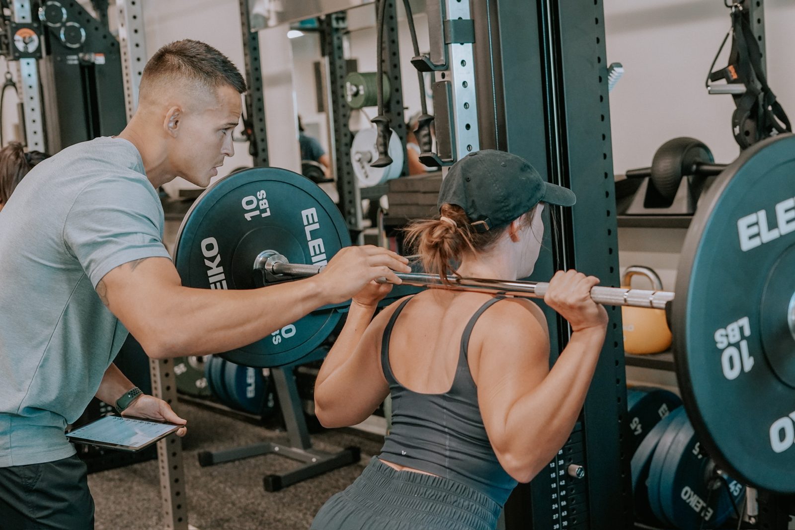 A proof3 coach spots a member during a barbell squat.
