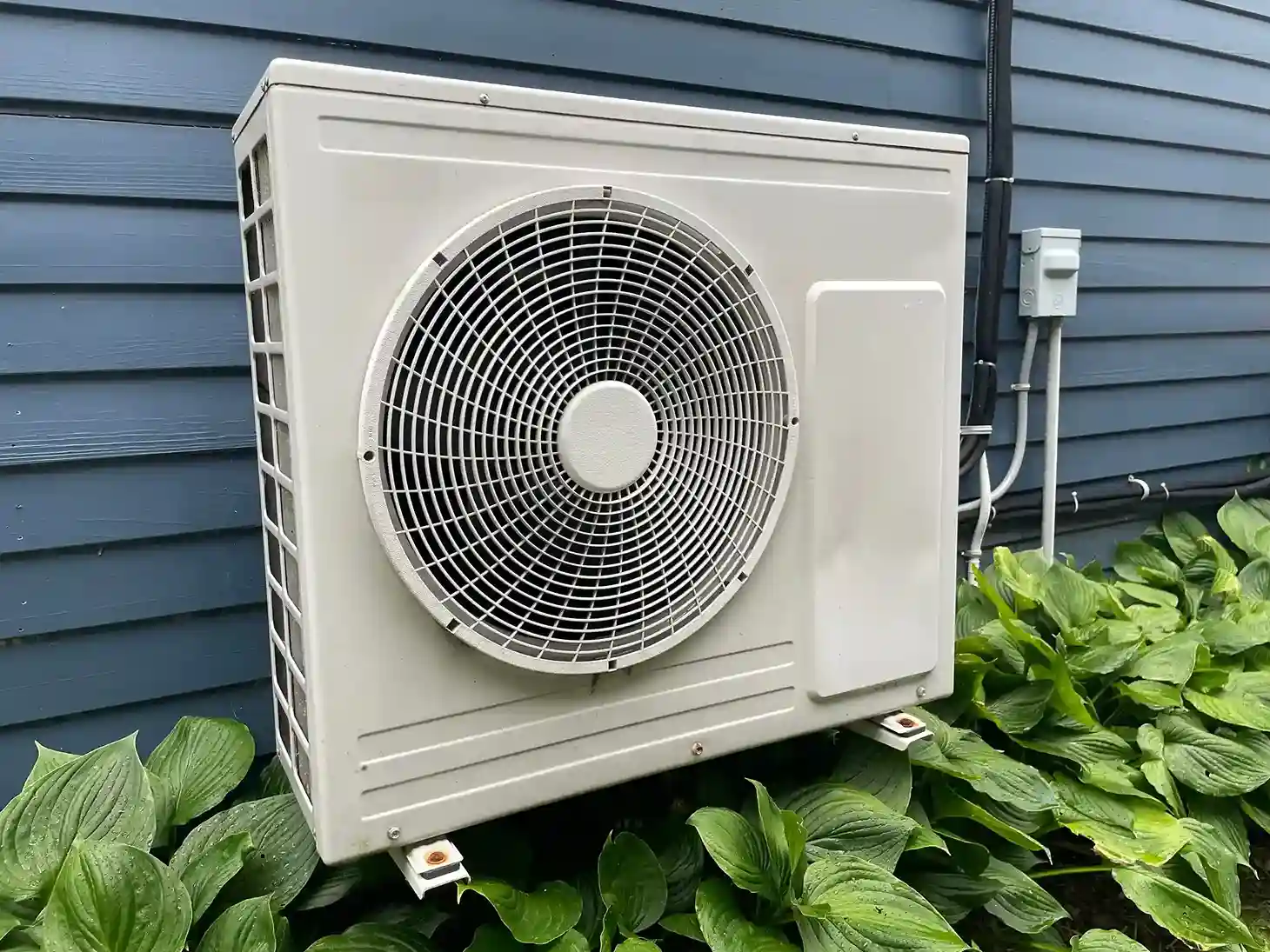 Outdoor air conditioning unit on blue house wall with surrounding green plants