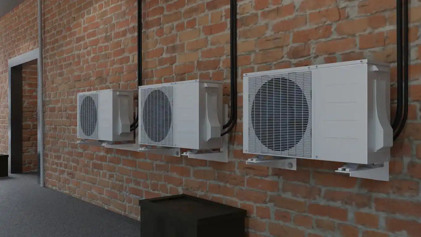 Three white air conditioning units mounted on brick wall with black cables and nearby doorway