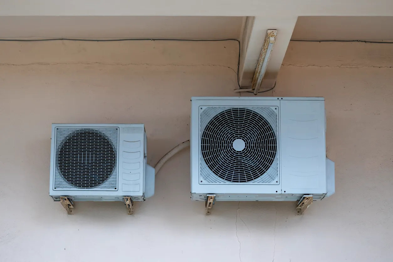 Two wall-mounted air conditioning units of different sizes with protective grilles and connected wiring