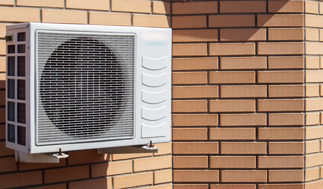 Rectangular outdoor air conditioning unit with circular fan on light brown patterned brick wall